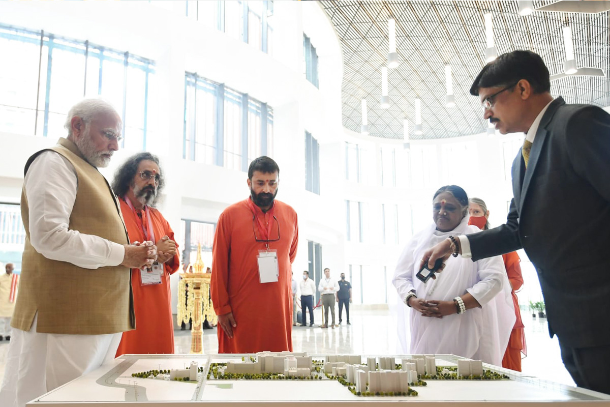 Amma, Swami Amritaswarupananda, Swami Nijamrita and PM Modiji watching as Dr. Sanjeev Singh, Group Medical Director, explains a model of the entire hospital complex.