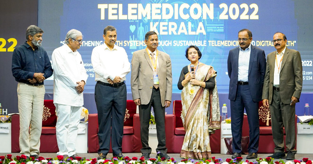 Professor Vidya Ramkumar, in a gold patterned sari, speaks with the mic in hand, alongside the members of the Telemedicine Society.