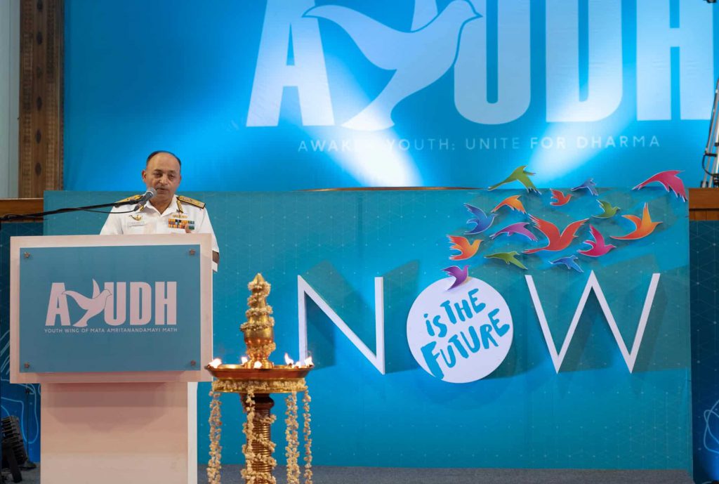 Vice Admiral Anil Kumar Chawla in white military dress addresses AYUDH from a podium with a blue background with the words "Now is the future"