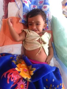 Athmika lying in bed at the hospital with a smile on her face.