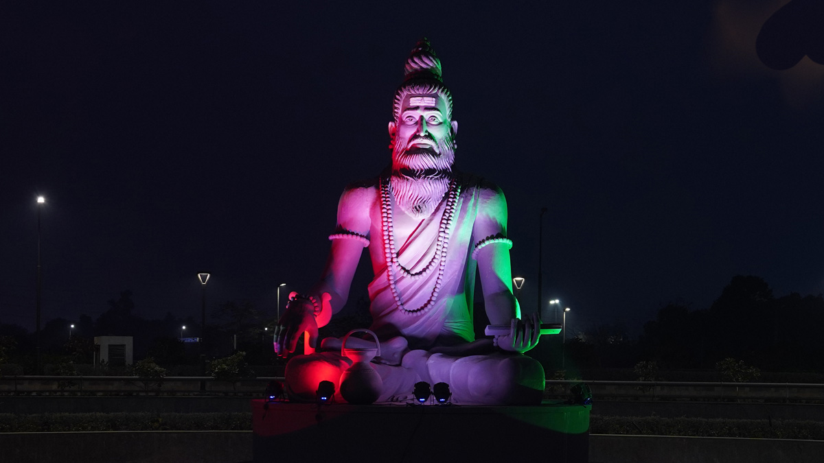 A statue of an ancient sage (Sri Sushrutha) with a beard and wearing traditional monk clothing. The statue is illumined with the G20 India colours of red, white and green.